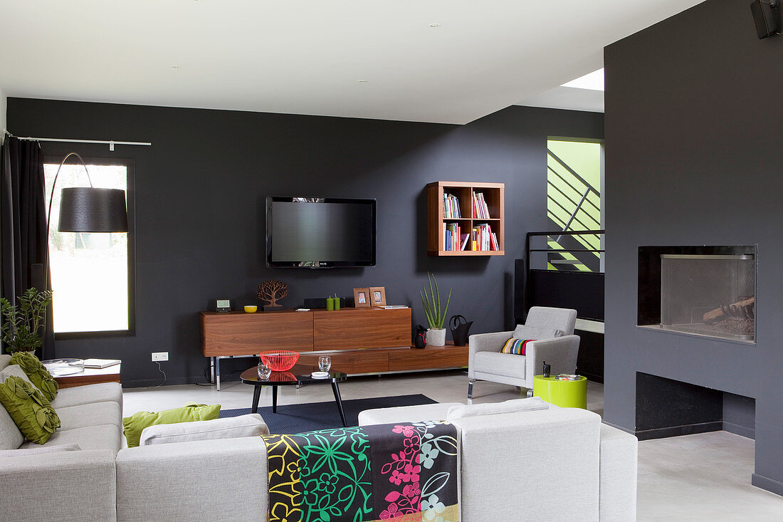 Kamin, Polstersofa, Coffeetable, Sideboard, Wandfernseher und Sessel im Wohnbereich mit dunklen Wänden