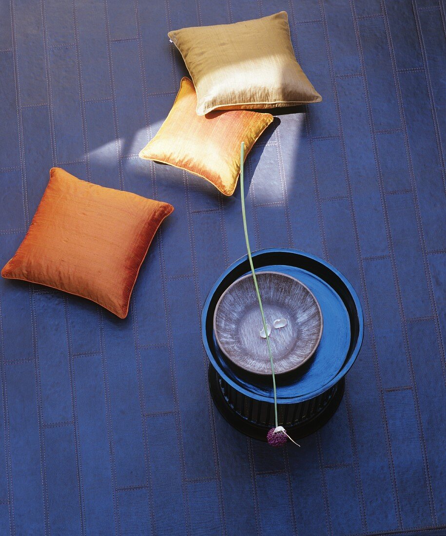 Elegant cushions, side table and allium flower lying across bowl on leather rug