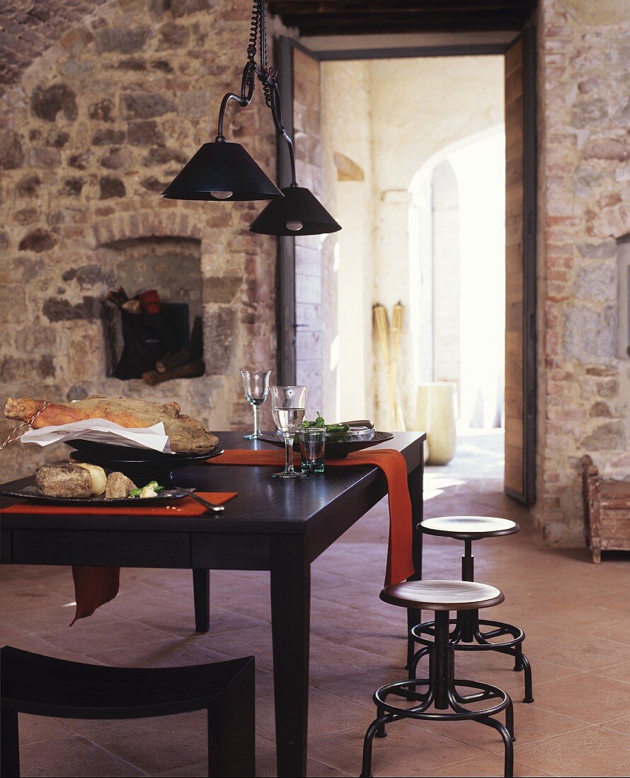 Set, black dining table and stools in front of open doorway in stone wall