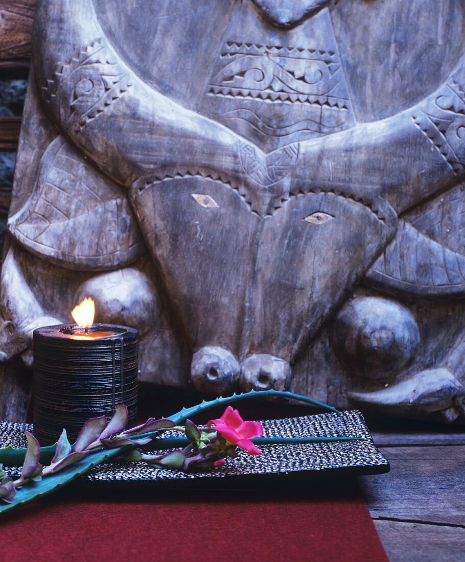 Lit candle in bowl and flower in front of ethnic carving