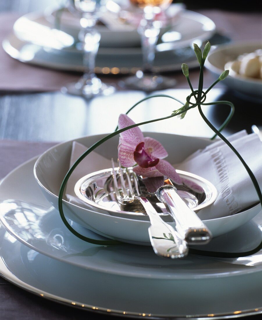 Edles Tischgedeck mit weißem Geschirr, Silberbesteck und Orchideenblüten