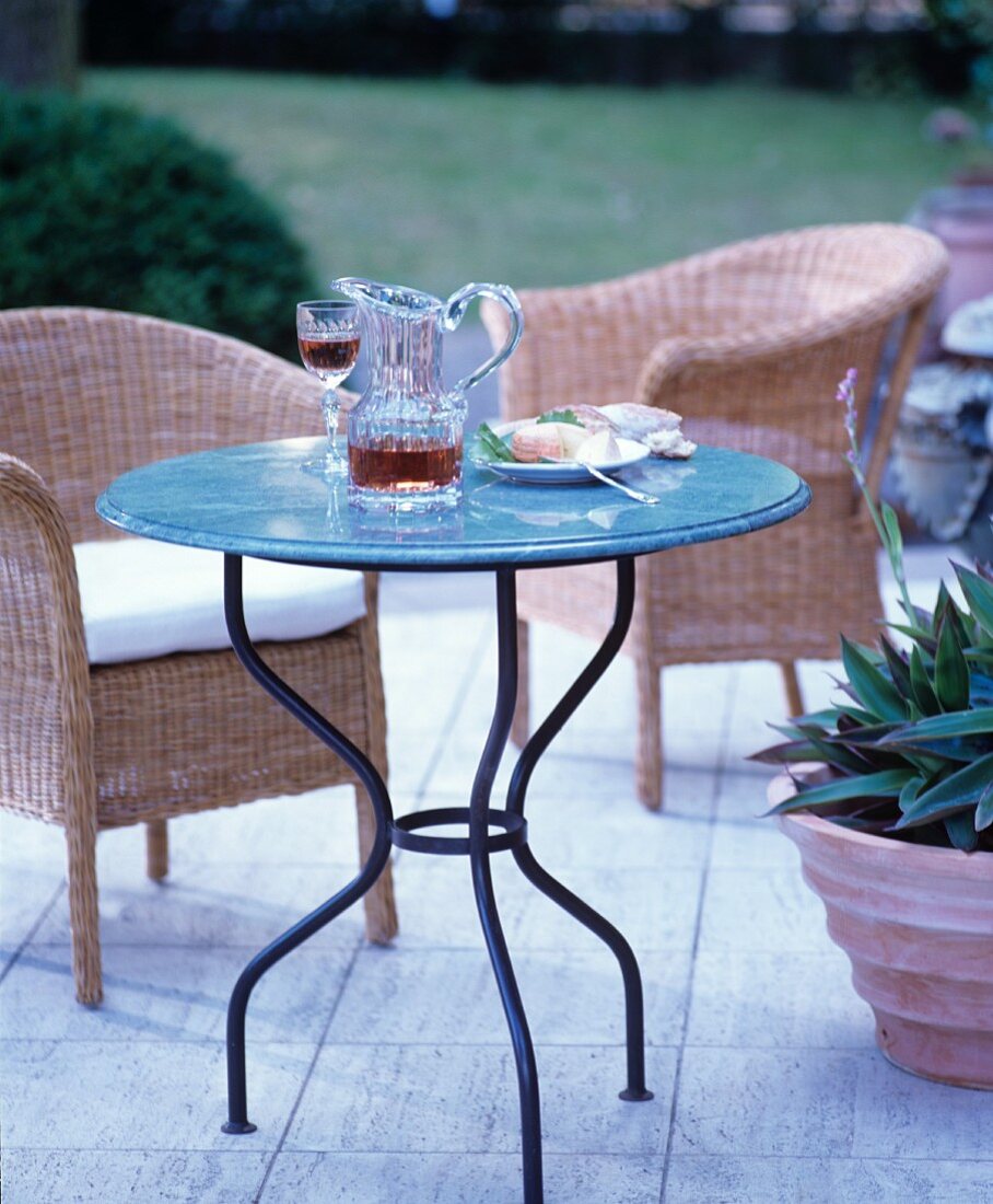 Runder Gartentisch mit Glaskrug auf Terrasse mit Korbstühlen