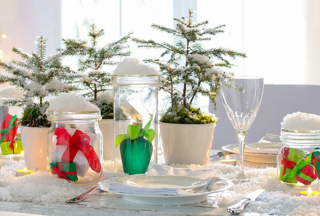 Dekoschnee, kleine Fichtenbäume und verpackte Geschenke in Einmachgläsern auf Weihnachtstisch