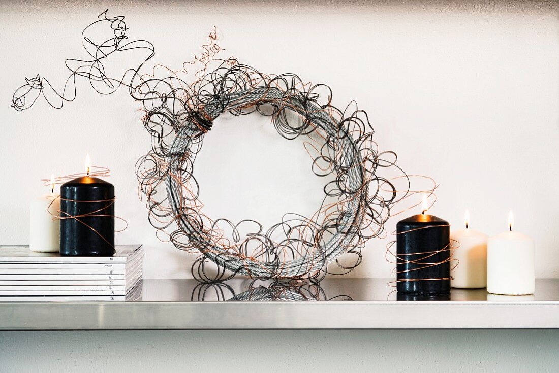 Decorative wreath hand-made from copper wire between lit, black and white candles