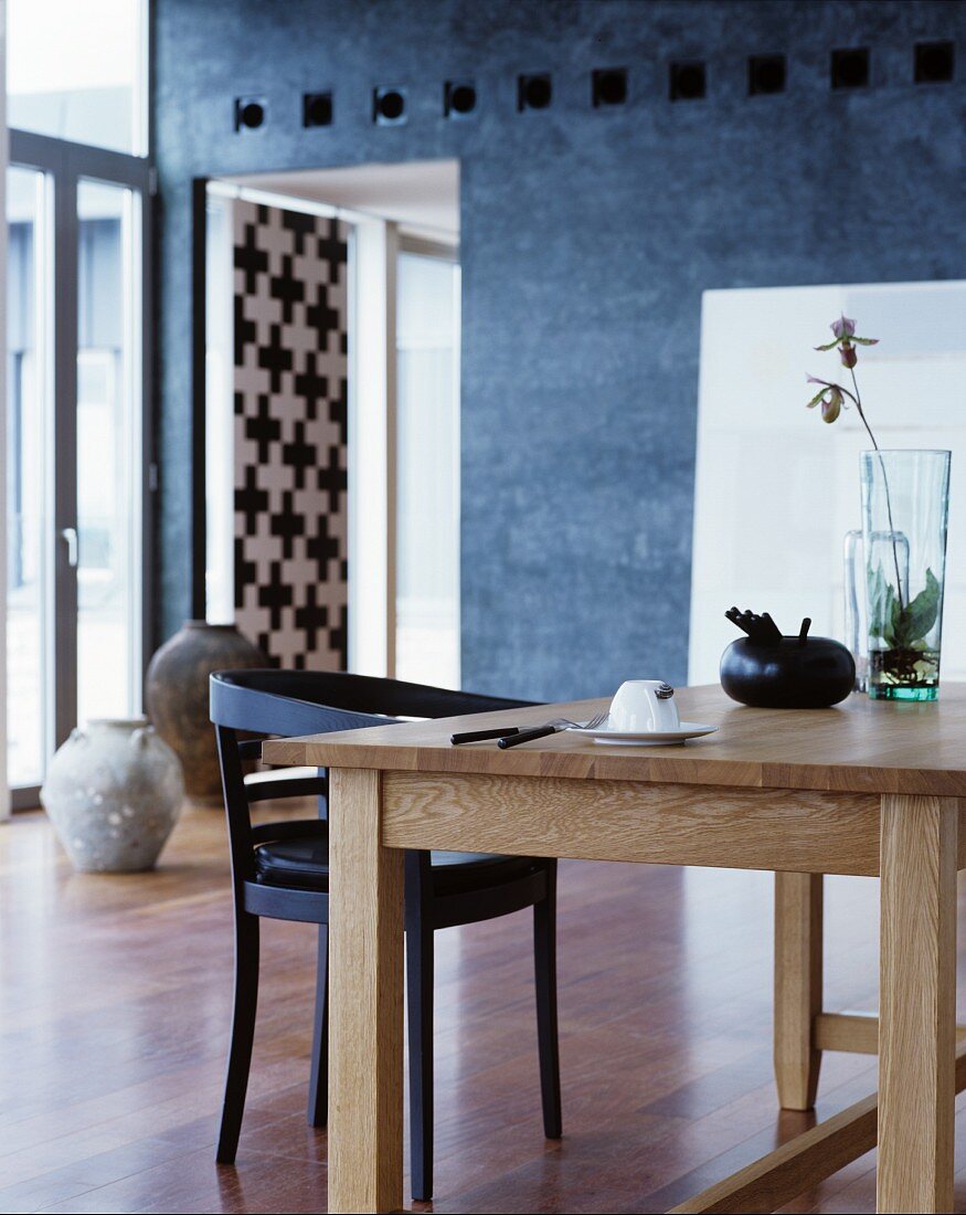 Schlichter Holztisch mit Glasvase und schwarzem Stuhl