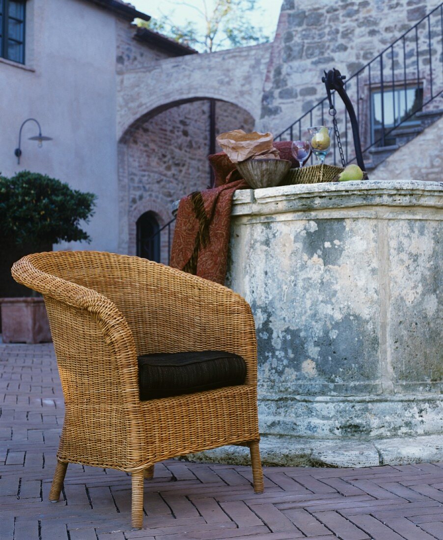 Korbsessel mit Sitzpolster vor Vintage Brunnen in mediterranem Innenhof