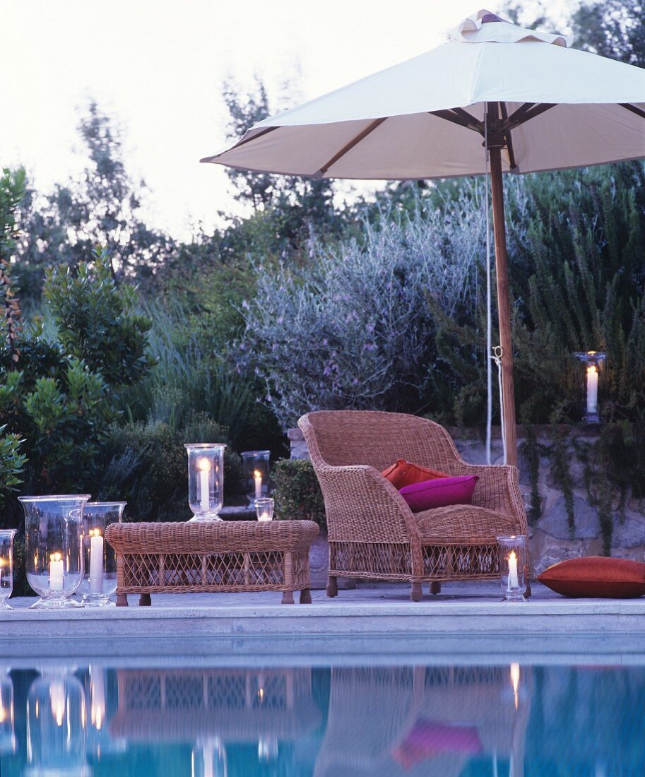 Romantische Abendstimmung am Pool mit gemütlichem Korbsessel und brennenden Windlichtern