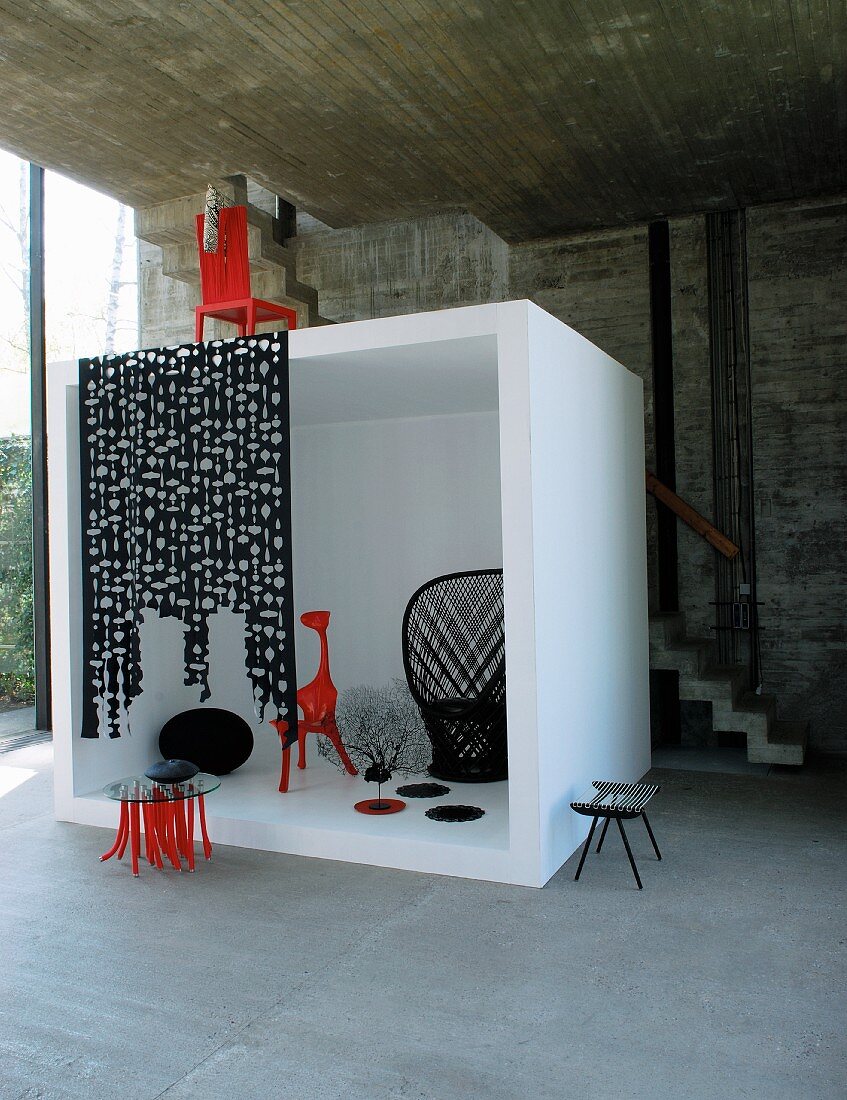 Black and red designer furniture in white cube in front of concrete wall