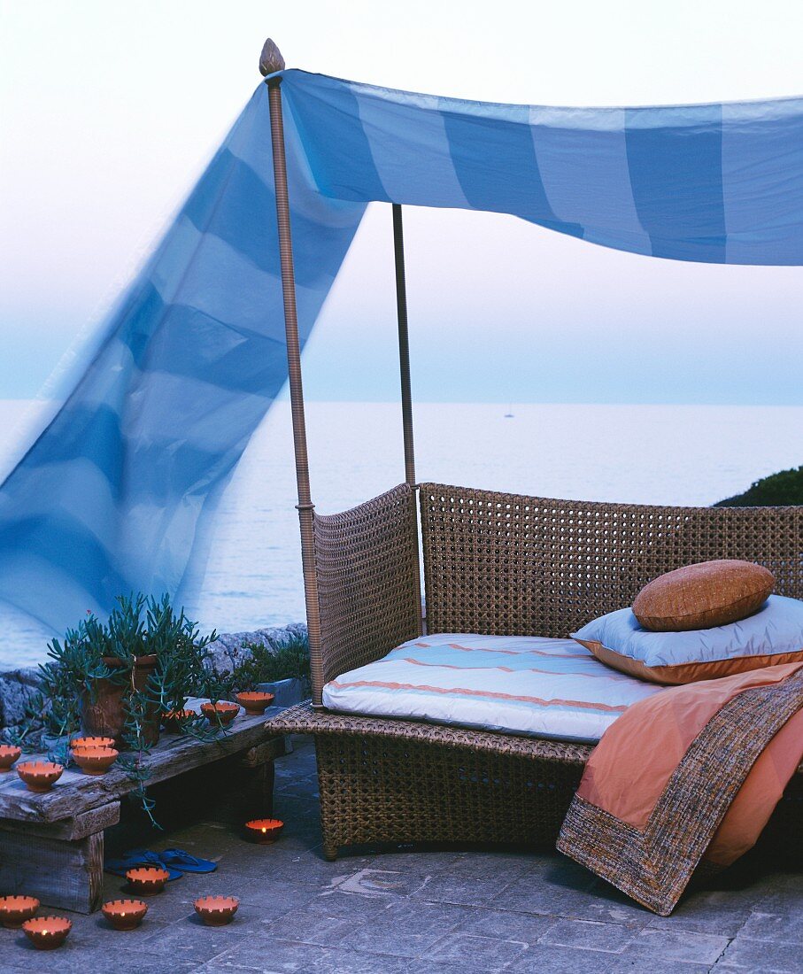 Couch below canopy surrounded by candles and with sea view