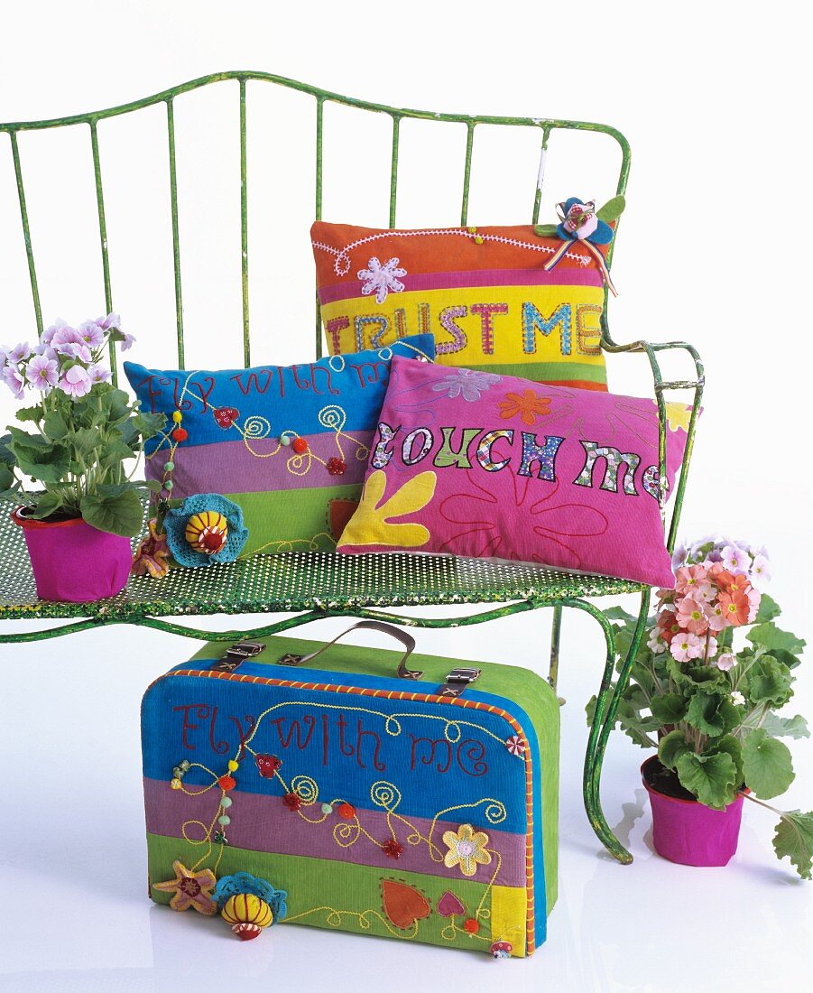 Colourful cushions and hippy-style suitcase on and around metal bench