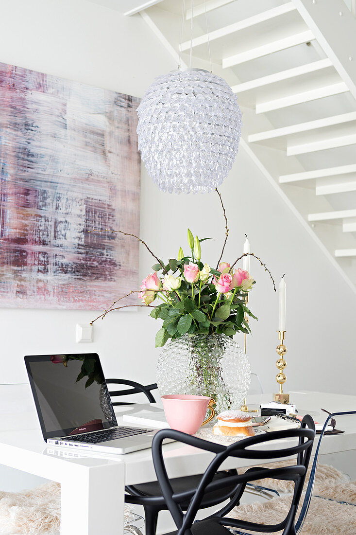 Weisser Tisch mit Rosenstrauß und Laptop und schwarzer Stuhl vor modernem Gemälde mit rosa Akzenten im Essbereich