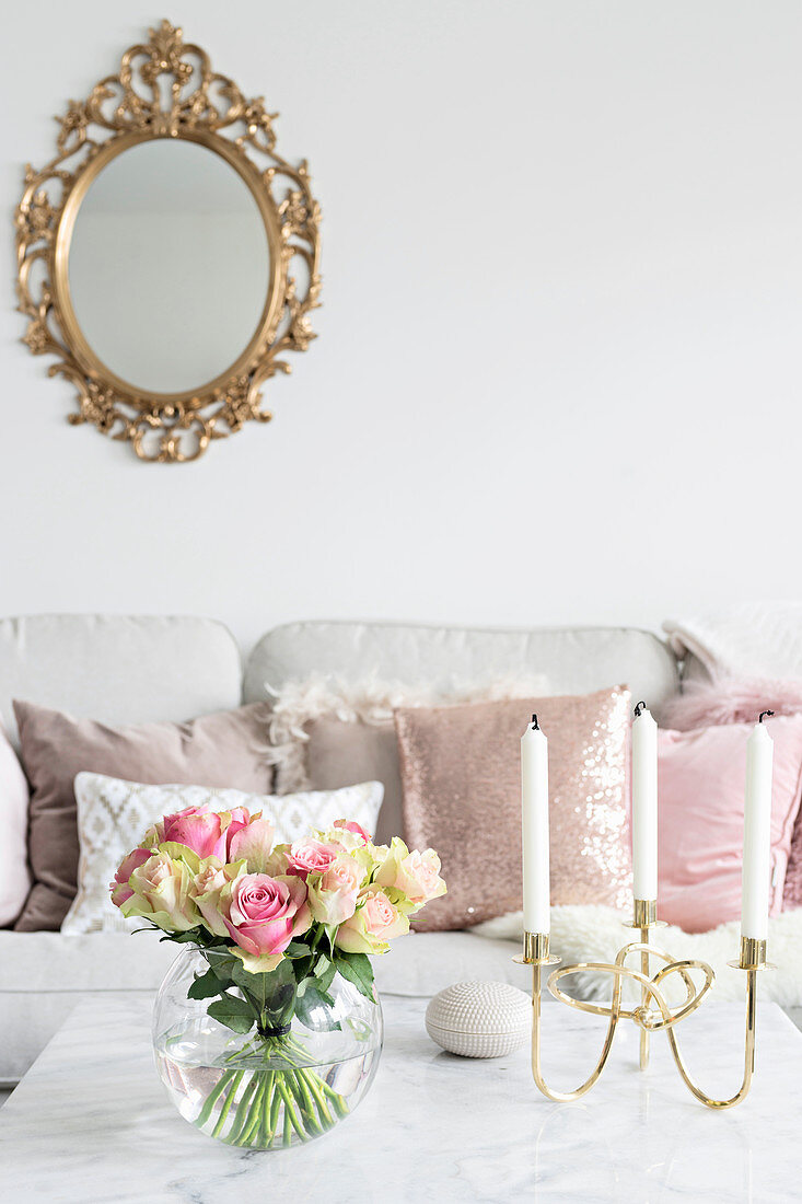 Rosenstrauß in Kugelvase und Kerzenhalter auf Couchtisch, im Hintergrund Goldrahmen-Spiegel über Sofa mit Dekokissen