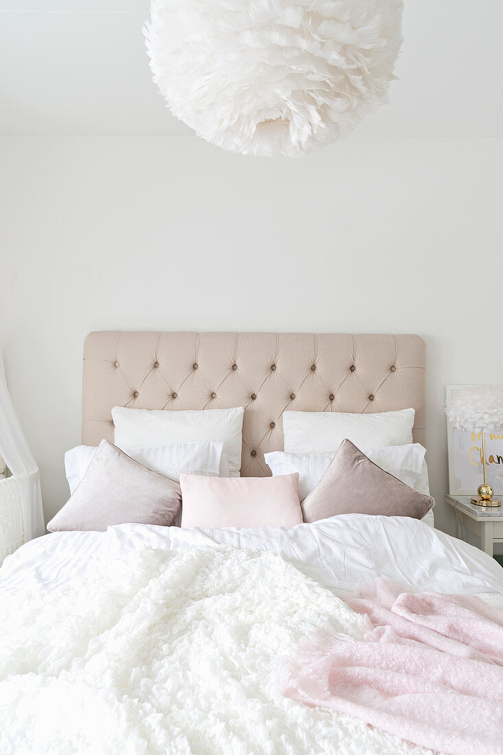 Double bed with button-tufted headboard in bedroom in white and pastel shades