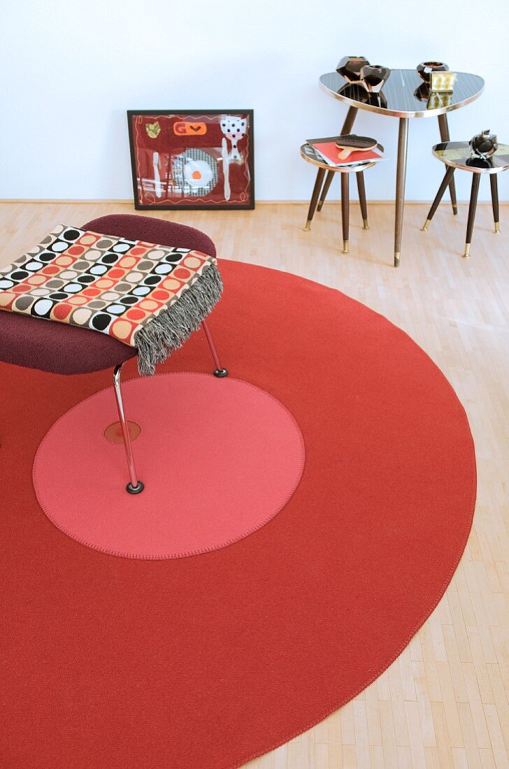 Hocker auf rundem Teppich neben drei Retro-Tischen