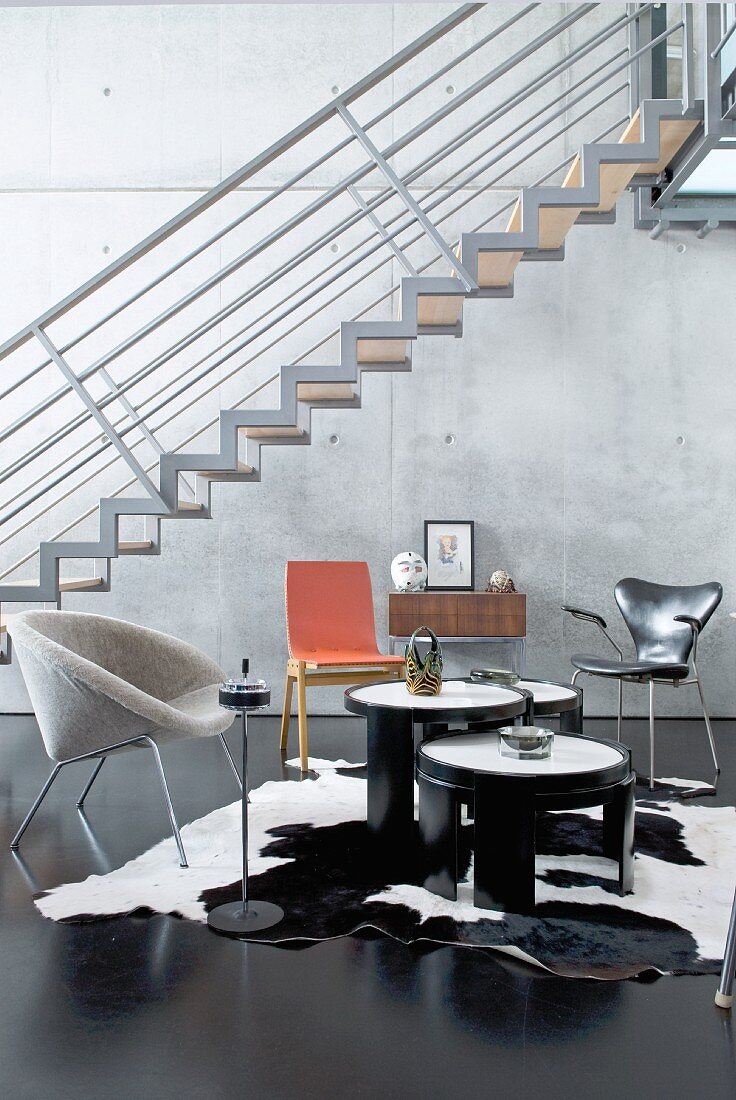 Designerstühle vor schwebender Treppe und Betonwand