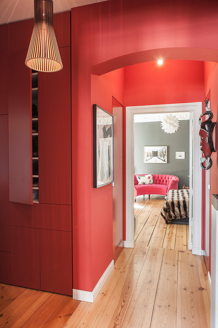 Red fitted cupboards in hallway with red walls and view into bedroom