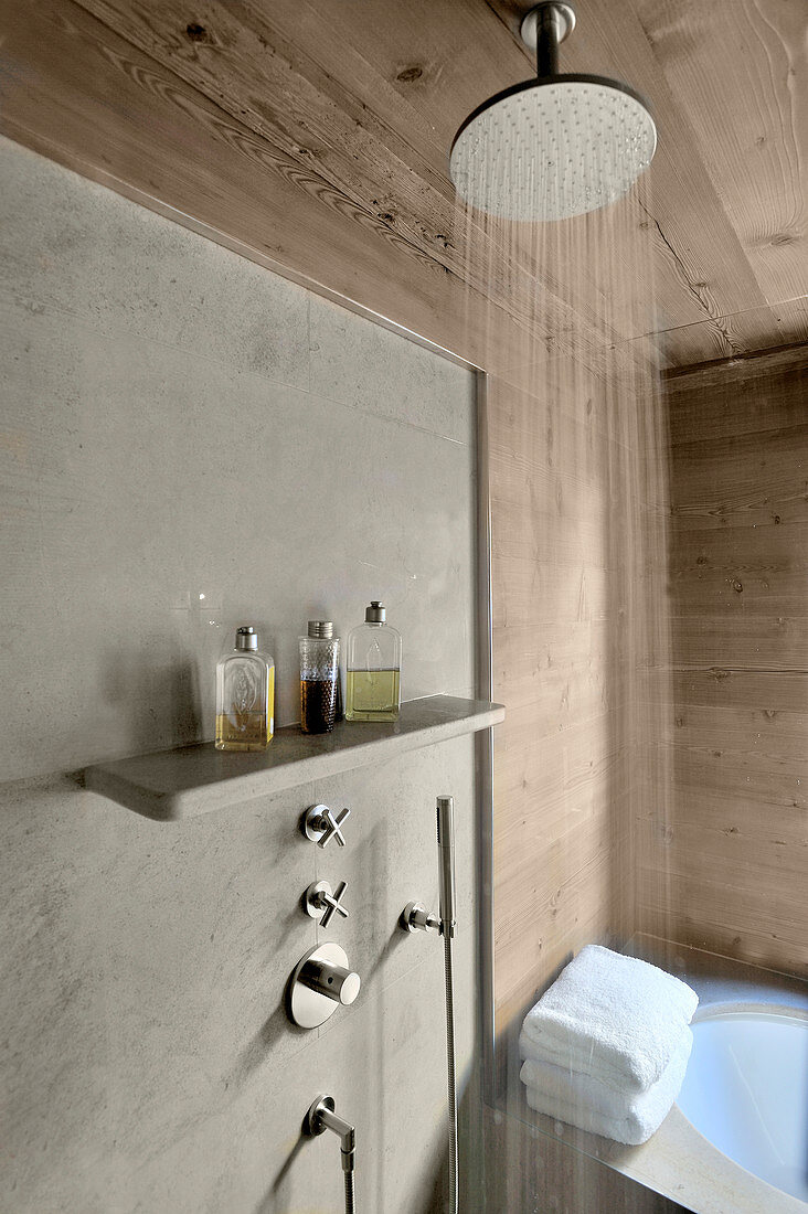 Rainfall shower in front of concrete shower wall in wood-clad bathroom