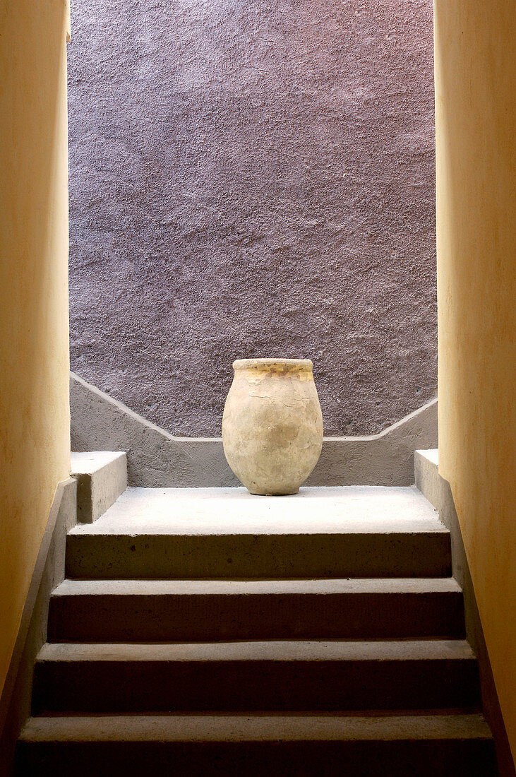 Ein alter Tontopf auf der Treppe vor lilafarbener Wand