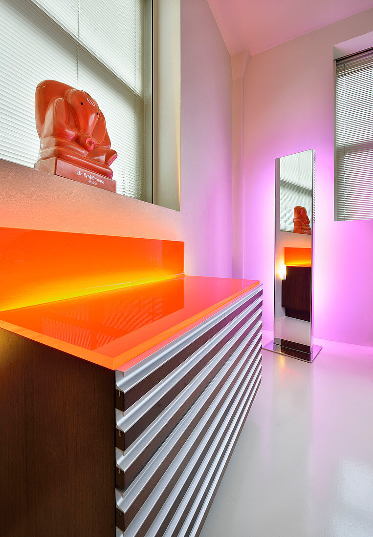Indirekte Beleuchtung in Orange und Pink an Spiegel und Kommode