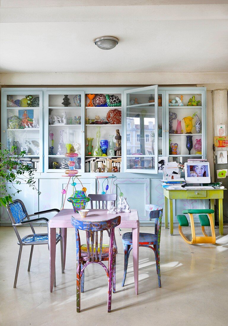 Table and colourful chairs in front of vases in glass-fronted cabinets