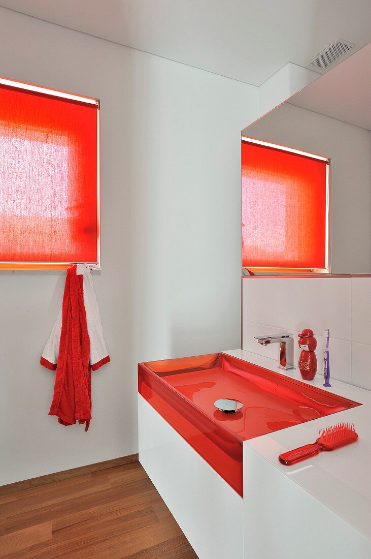 Modernes Bad mit transparentem Waschbecken und roten Akzenten