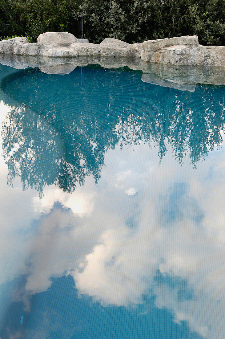 Blauer Himmel und Wolken spiegeln sich im Pool mit Steinbegrenzung