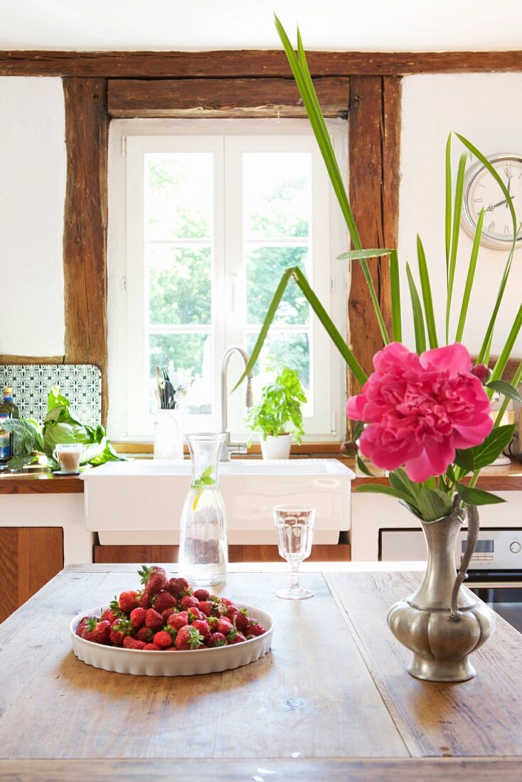 Erdbeeren, Wasserkaraffe und Zinnvase mit Pfingstrose auf Küchentisch