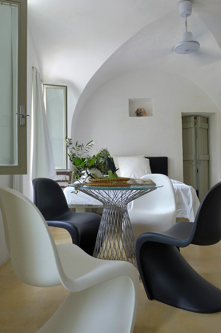 Schwarze und weiße Pantonstühle um runden Tisch mit Glasplatte in Zimmer mit historischem Flair
