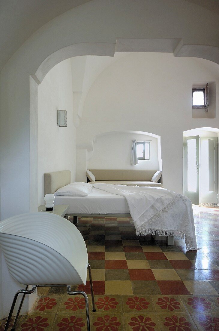 Restauriertes Schlafzimmer in historischem Gebäude mit weißem Designerstuhl auf Fliesenboden