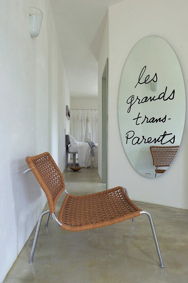 Motto on oval mirror and easy chair in front of hallway with view into bedroom