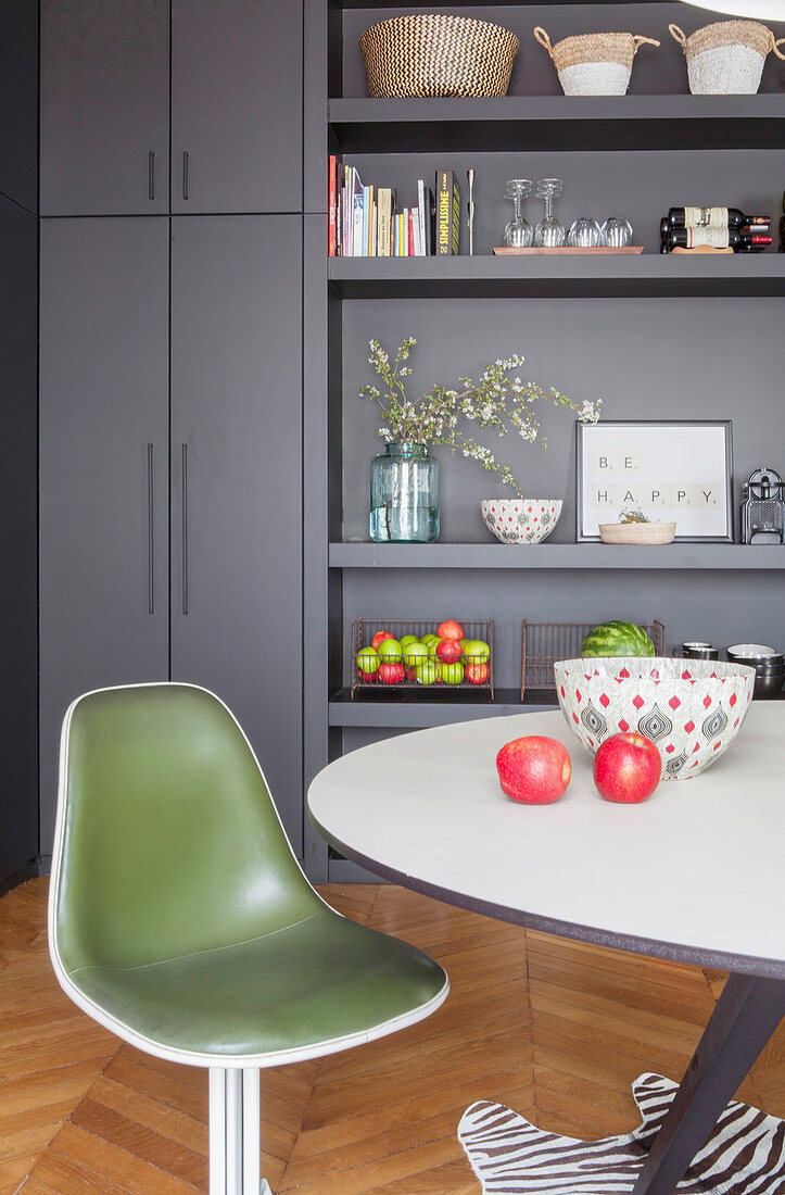 Green, retro shell chair in front of grey fitted cupboards and shelves