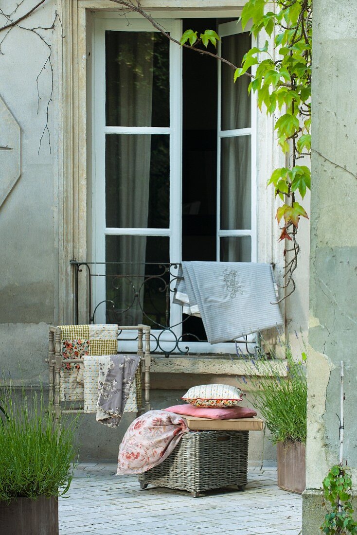 Korbkiste und Stummer Diener mit Kissen und Stoffen vor französischem Fenster im Innenhof