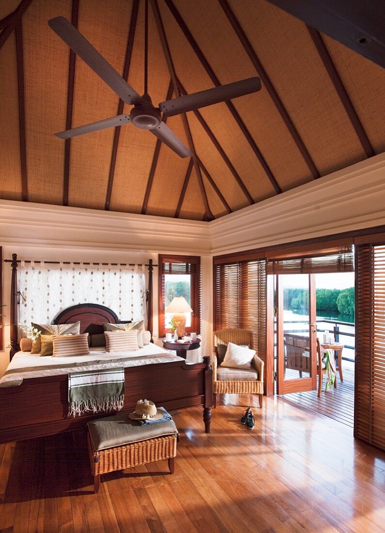 Doppelbett und Korbmöbel in elegantem, hohem Schlafzimmer mit Balkon