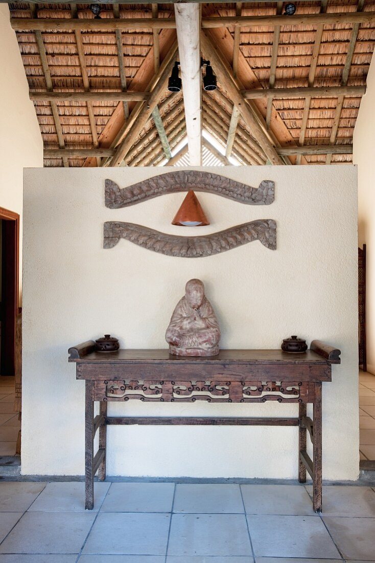 Buddhafigur auf antikem Holztisch vor Wandscheibe
