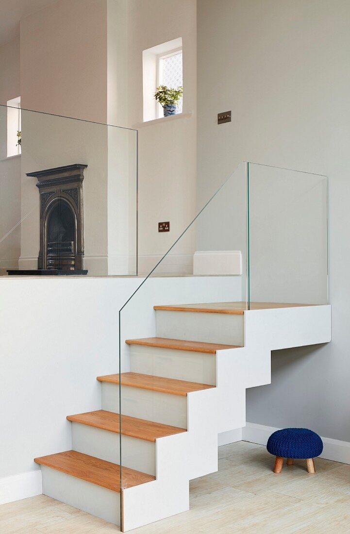 Staircase with glass balustrade in interior with traditional fireplace