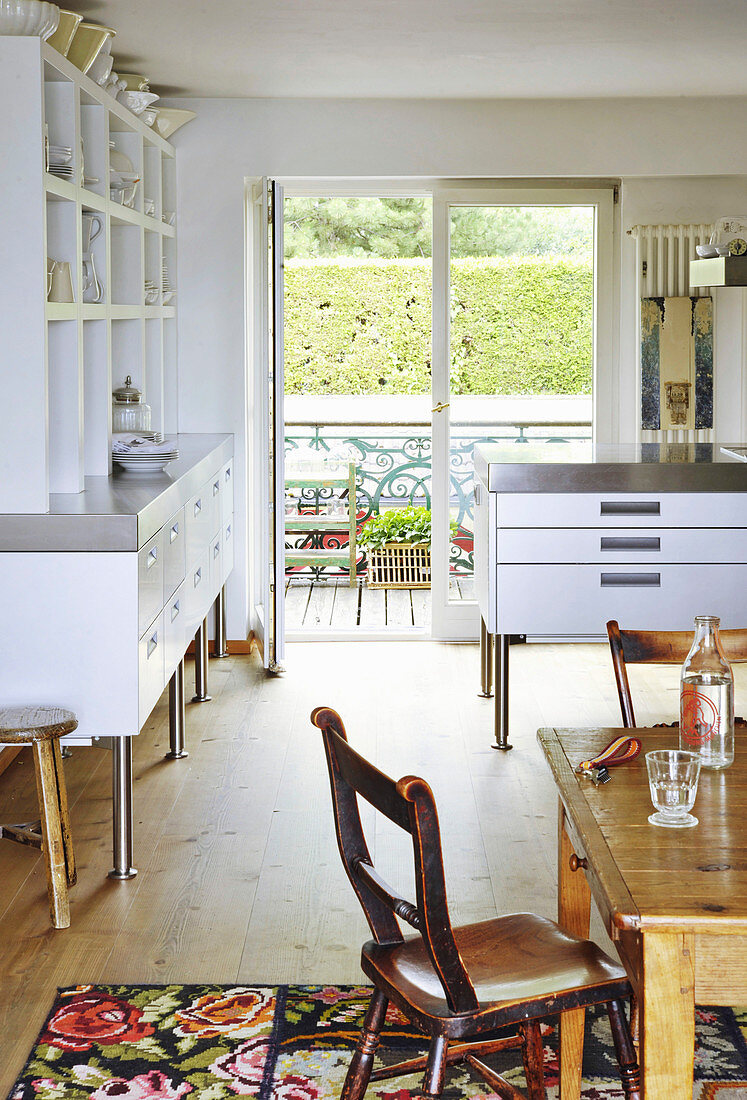 Rustikaler Holztisch und weiße Anrichte mit offenem Regal in der Küche, Blick durch geöffnete Tür auf Balkon