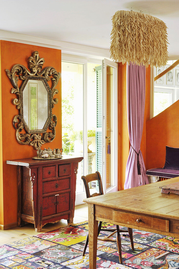 Brockspiegel und chinesischer Kommode vor orangefarbener Wand, Lampe aus Kokosfasern über Esstisch