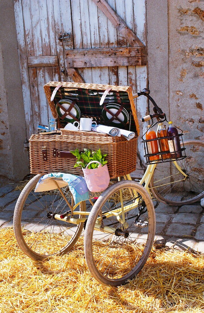 Picknickkoffer auf einem Dreirad vor einer Scheune mit Stroh