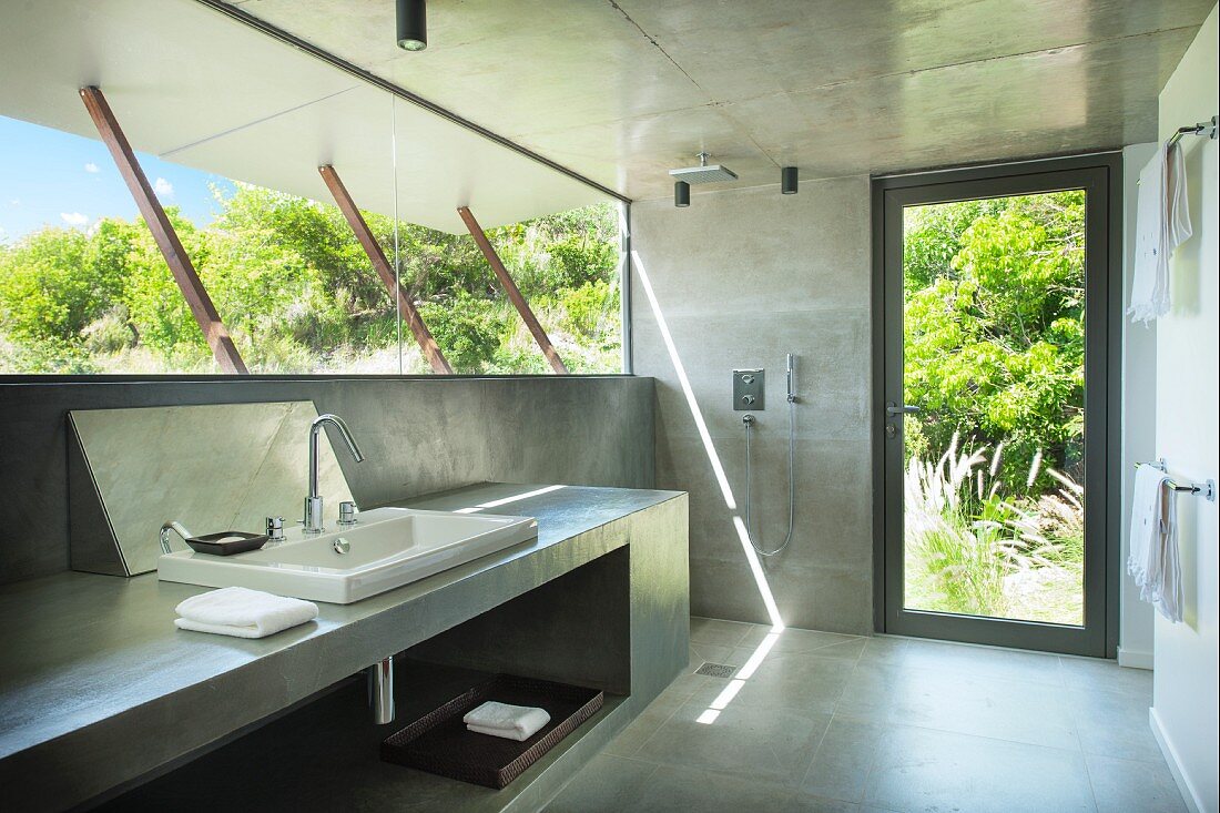 Concrete bathroom with glass wall and view into green garden