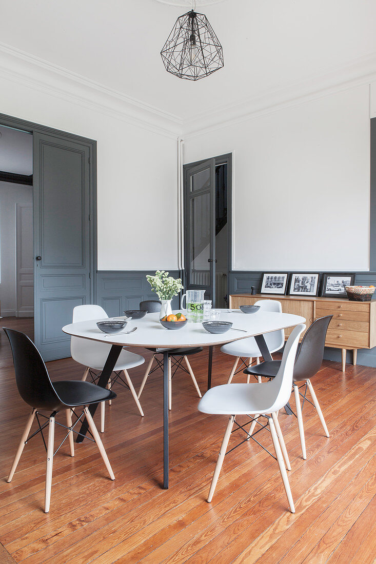 Esstisch mit Stühlen im Wohnraum mit weissen Wänden und grau-blauer Vertäfelung im Sockelbereich