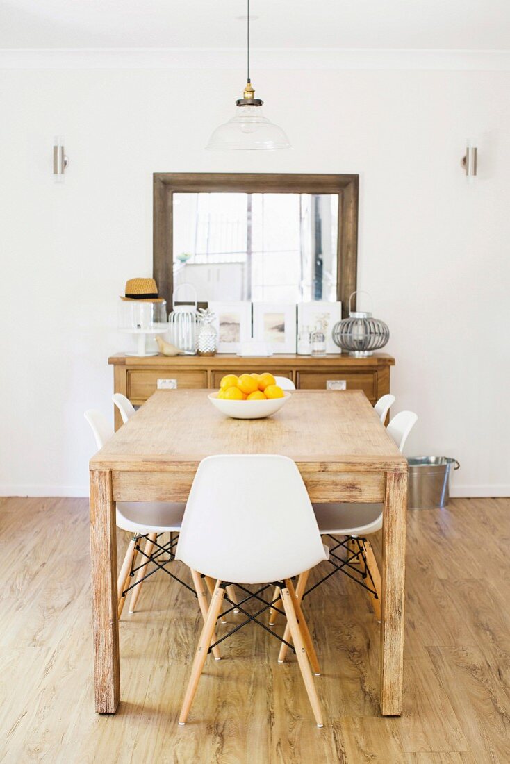 Rustikaler Holztisch mit weissen Schalenstühlen, im Hintergrund Konsolentisch und geramter Wandspiegel