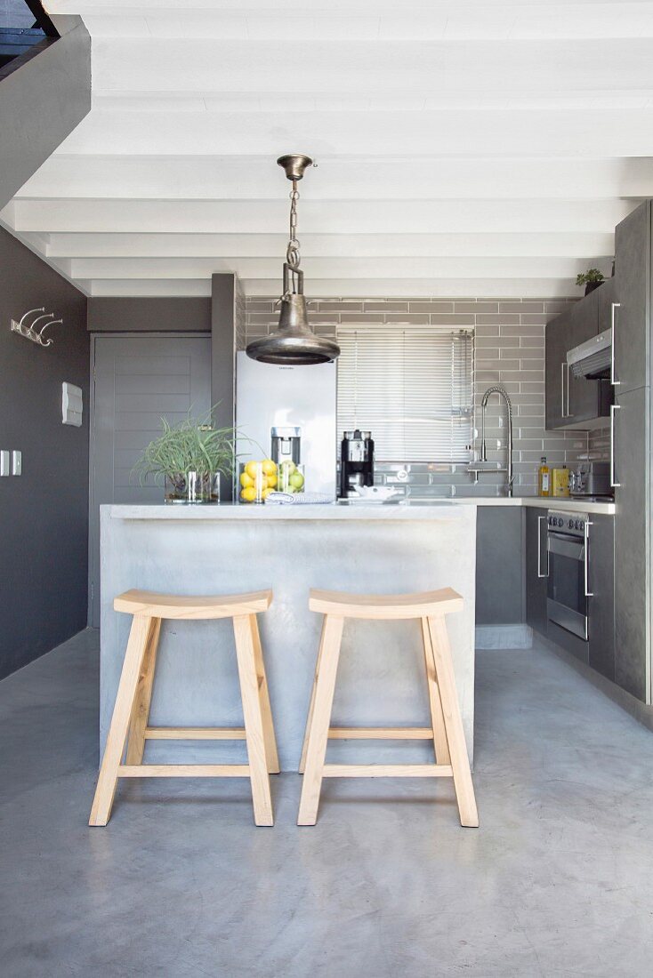 Küche in grauen Tönen, im Vordergrund Holzhocker an Frühstückstheke