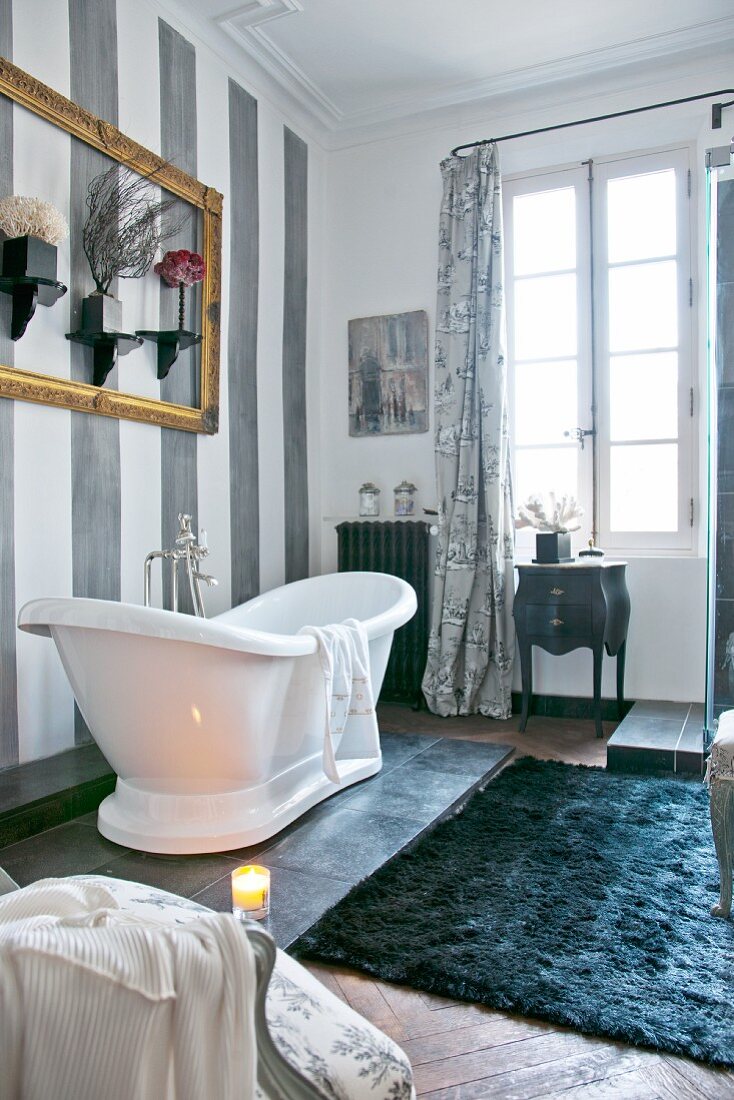 Wohnliches Badezimmer mit weißer, freistehende Badewanne vor grau gestreifter Wand und Sprossenfenster