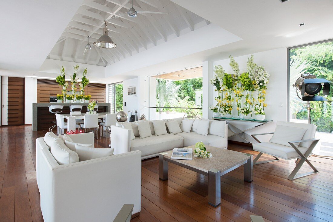 White designer furniture and opulent flower arrangements in open-plan living area of beach house