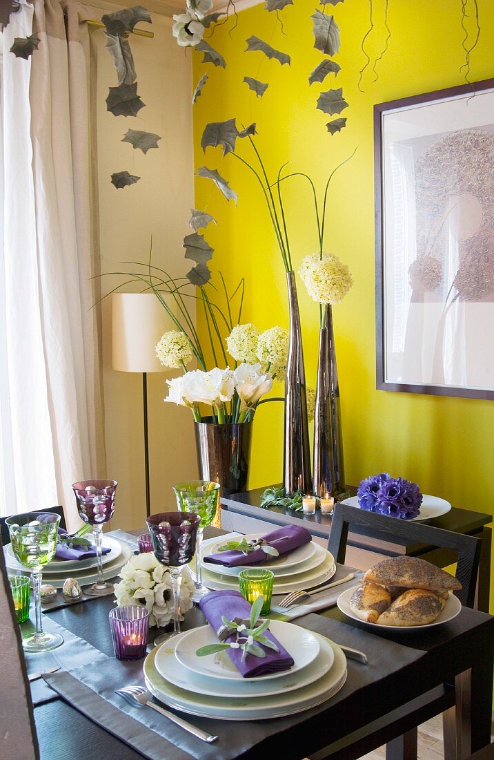 Festively set dining table in front of flower arrangement and yellow wall