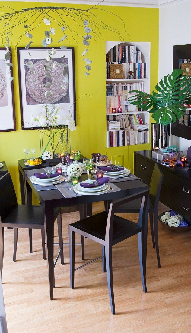 Festlich geschmückter Esstisch mit Teelichtern, weiße Kunstblumen auf Konsolentisch vor gelber Wand