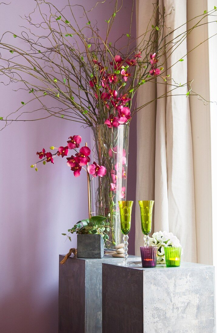 Dekoratives Kunstblumen-Arrangement mit grünen Sektgläsern und Teelichtern