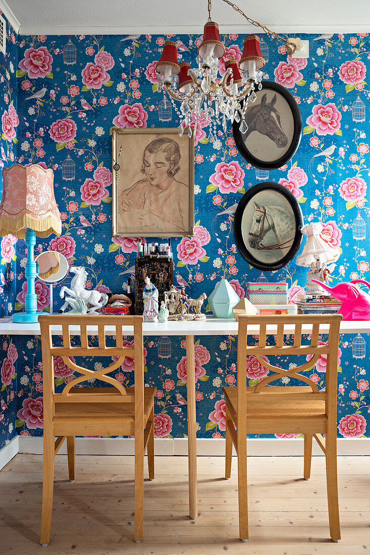 Ornaments on table and two chairs in front of pictures on floral wallpaper