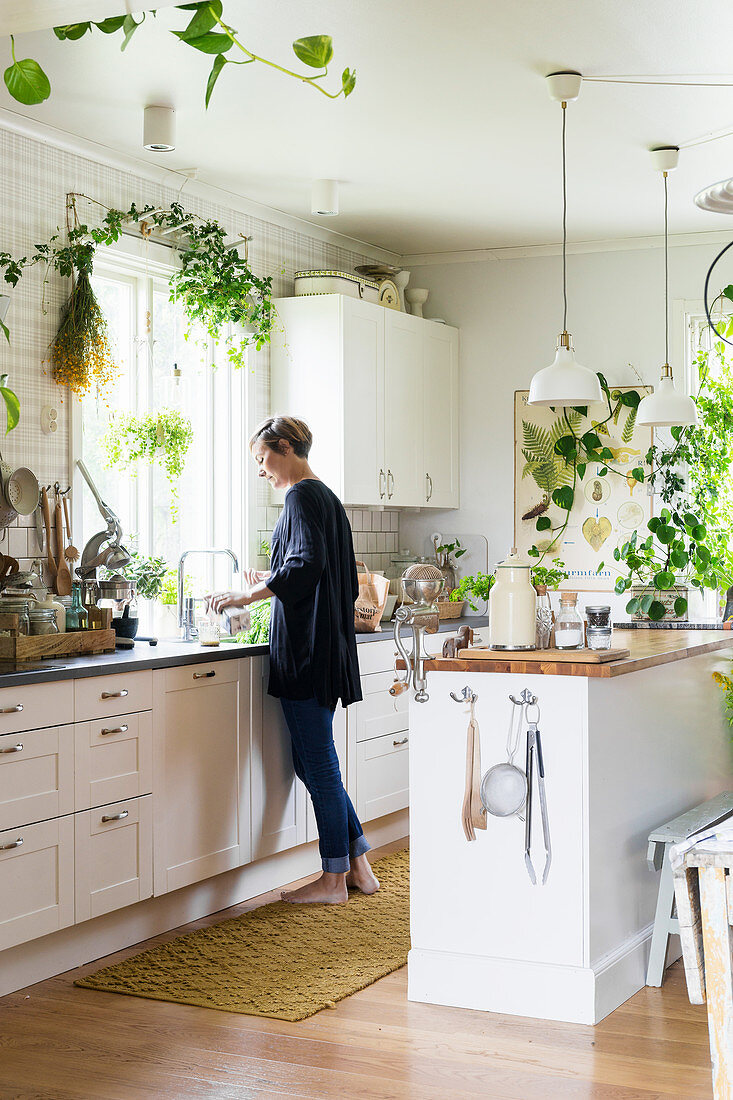 Frau steht in weißer Küche mit vielen Zimmerpflanzen