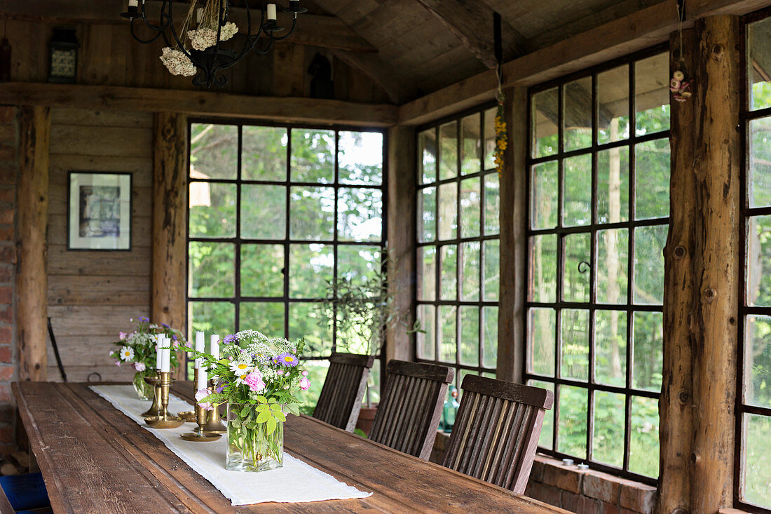 Großer Holztisch mit Stühlen in rustikaler Orangerie mit Sprossenfenster